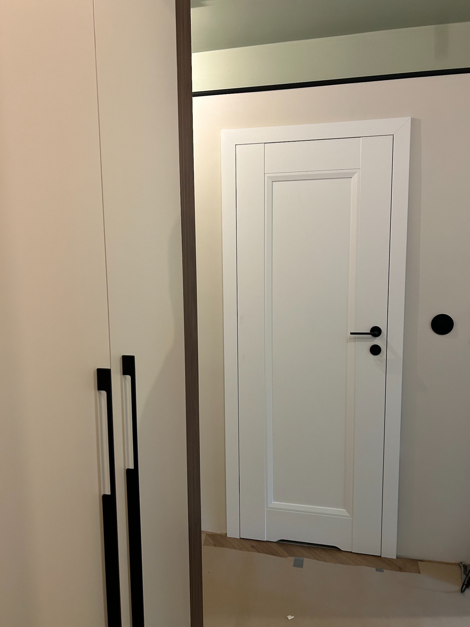 Białe drzwi wewnętrzne z czarną klamką, widoczne w lustrzanym odbiciu szafy w Żorach. Klasyczny design z prostokątnymi panelami i minimalistycznym wykończeniem.