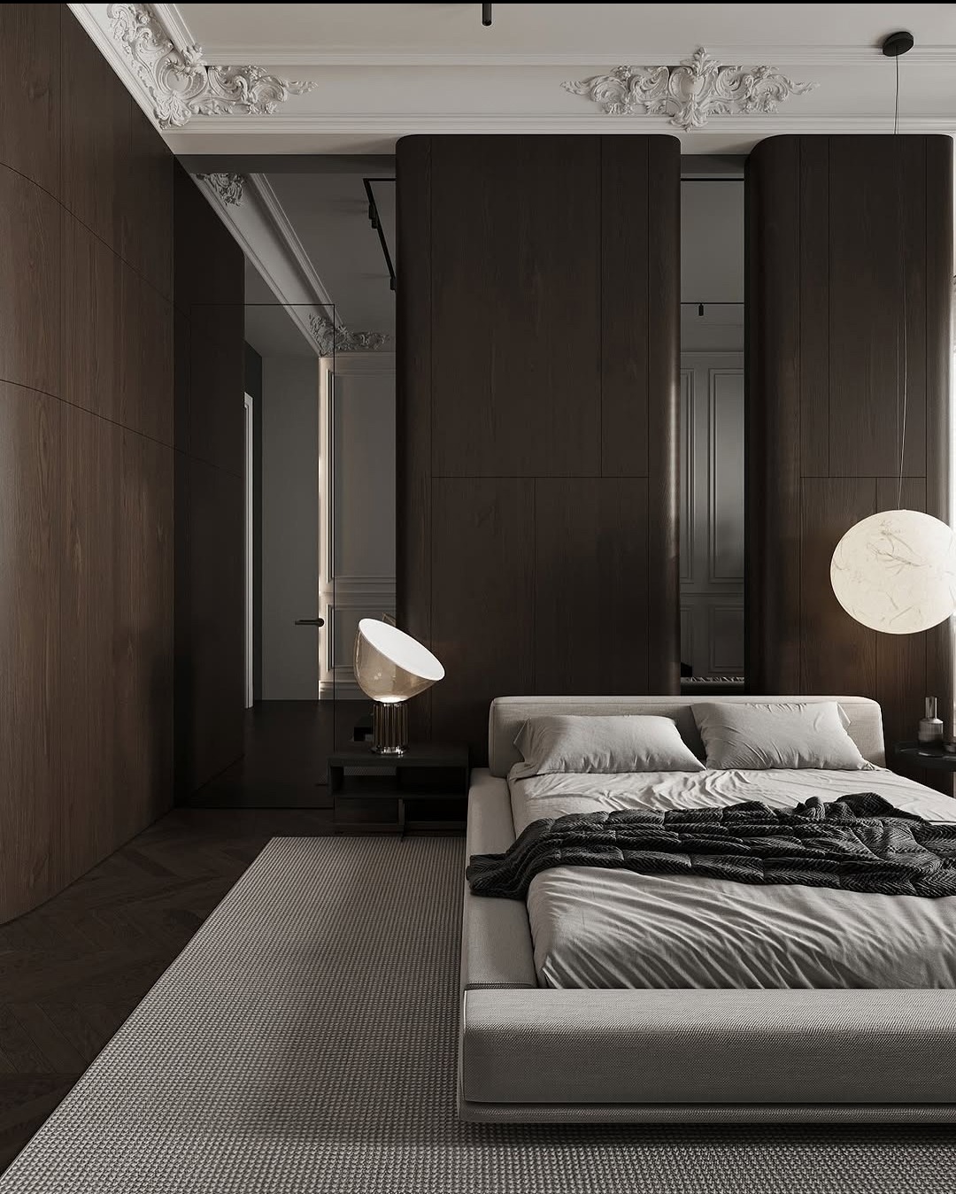 Nowoczesna sypialnia w odcieniach szarości i brązu z dużym łóżkiem, lampką nocną i wzorzystym dywanem. Dekoracyjne sztukaterie sufitowe dodają elegancji.