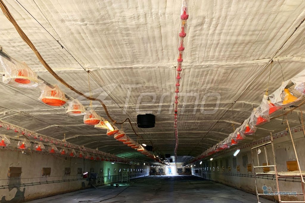 Poddasze budynku gospodarczego po natrysku pianką PUR; widoczne elementy wyposażenia zabezpieczone folią, równomierna struktura izolacji na całej powierzchni.