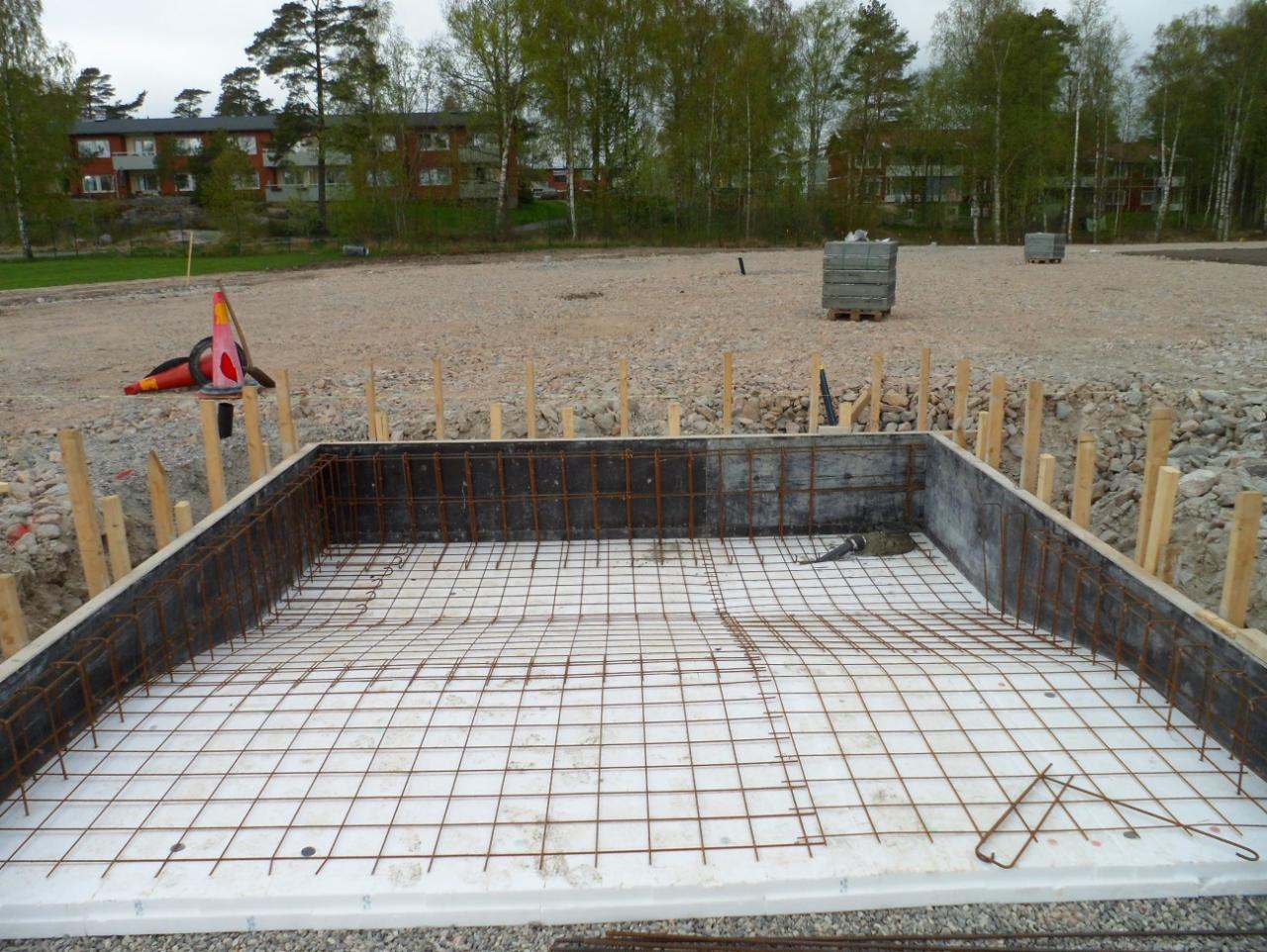 Przygotowanie fundamentów: zbrojenie na białym styropianie w szalunku, widoczne drewniane podpory i gruz na placu budowy.