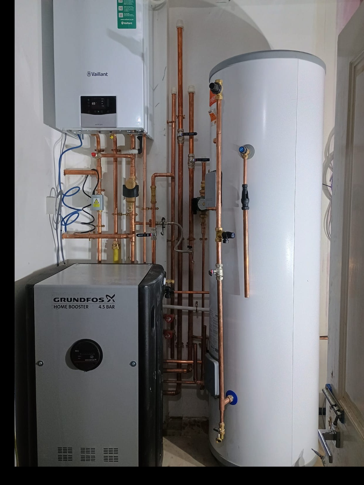 Nowoczesna kotłownia z piecem gazowym Vaillant, zasobnikiem wody i pompą Grundfos. Widoczne miedziane rury instalacji grzewczej i wodnej.