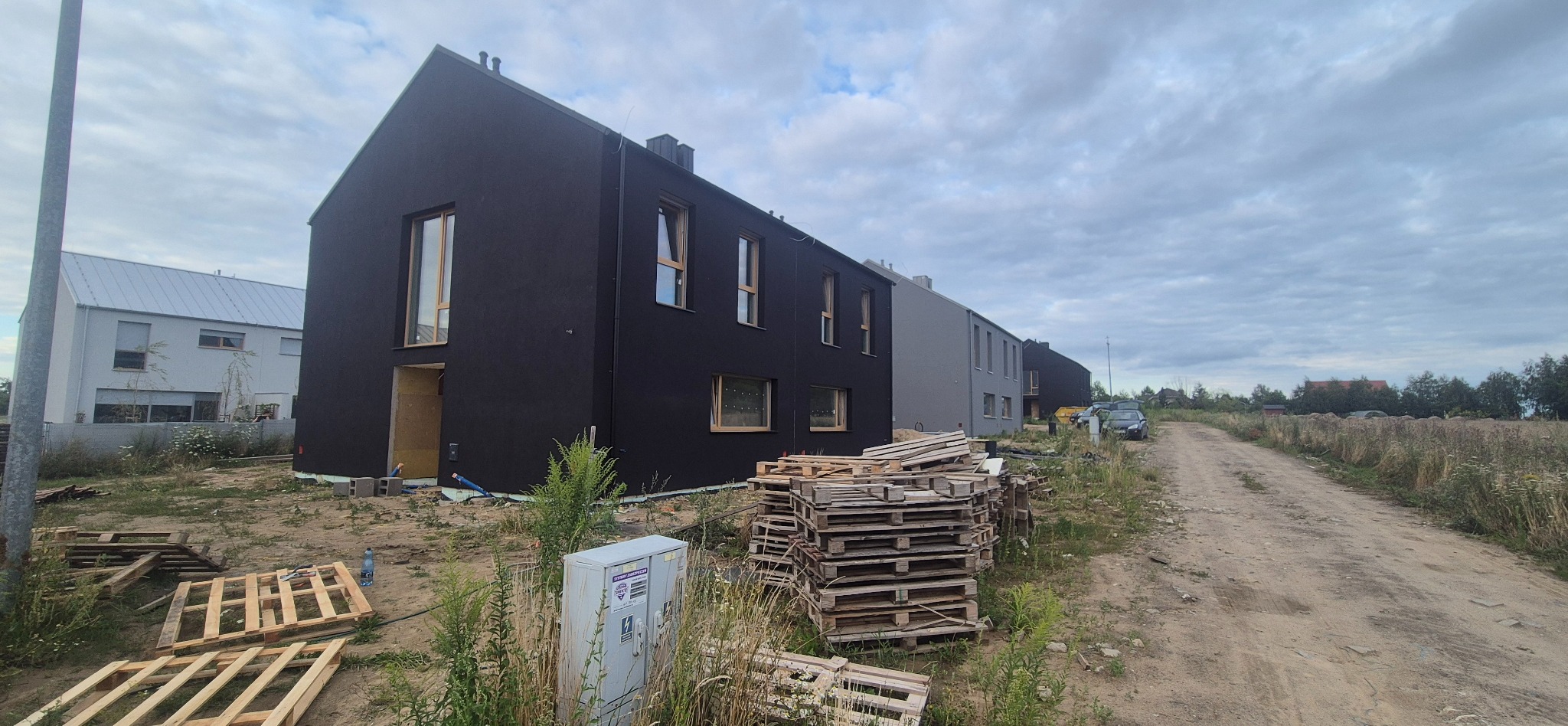 Nowoczesne domy szeregowe z elewacją w odcieniach szarości i czerni, palety na pierwszym planie, budowa w toku, pochmurne niebo.