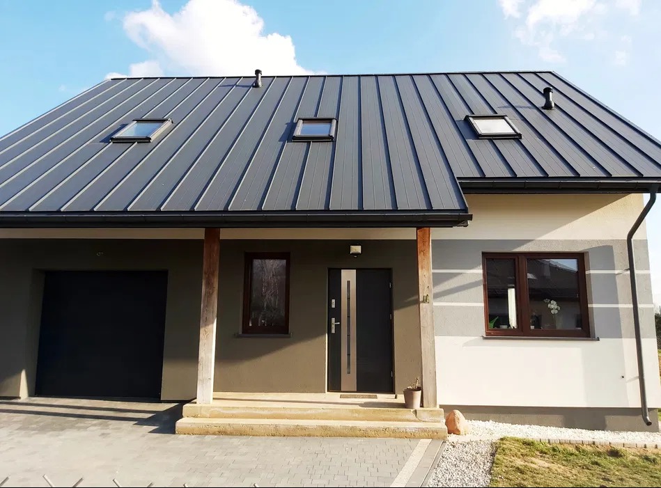 Nowoczesny dom jednorodzinny z szarą blachodachówką i elewacją w odcieniach beżu i bieli, z widocznym wejściem i garażem. Ujęcie w słoneczny dzień.