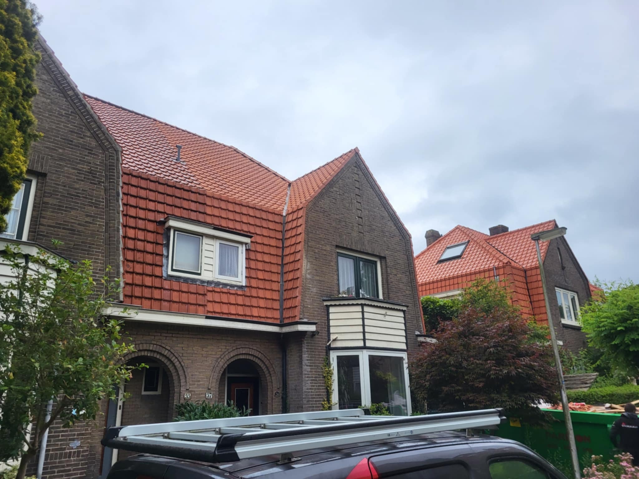 Domy z czerwonymi dachami w zabudowie szeregowej, widziane z dołu, z fragmentem samochodu z drabinką na dachu. Pochmurne niebo.