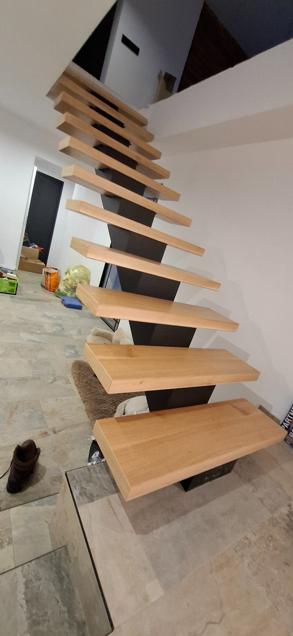 Nowoczesne schody z drewnianymi stopniami i czarną, metalową konstrukcją nośną, widoczne z dołu, w jasnym wnętrzu. Minimalistyczny design.