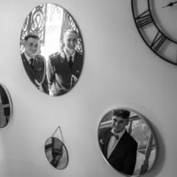 Czarno-białe odbicie w lustrach: dwóch mężczyzn w mundurach i jeden w garniturze, na ścianie zegar z rzymskimi cyframi. Nietypowe ujęcie.