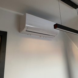 Feniks Kędra Krzysztof - Biały klimatyzator Rotenso zamontowany na ścianie w jasnym wnętrzu, widoczna czarna lampa sufitowa. Minimalistyczny design, nowoczesne rozwiązanie chłodzące.