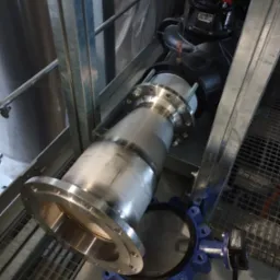 Instalacja przemysłowa z metalowymi rurami i zaworami w Będzieszynie. Elementy połączone spawami i śrubami, widoczne na tle metalowej konstrukcji.