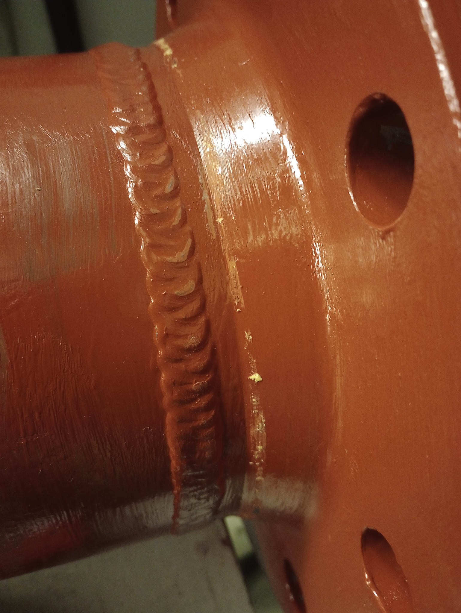 Bursztynowa, metalowa konstrukcja połączona spoiną. Widoczna faktura farby i ślady po procesie spawalniczym. Element z otworami montażowymi.