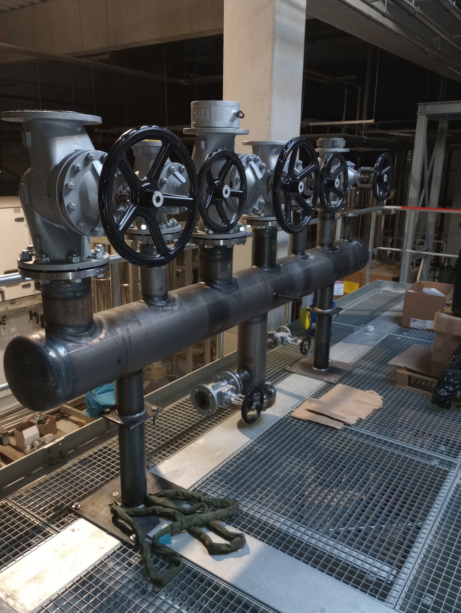 Metalowa instalacja przemysłowa z zaworami i rurami, spawana konstrukcja na ruszcie, widoczne ślady obróbki metalu, surowy industrialny wygląd.