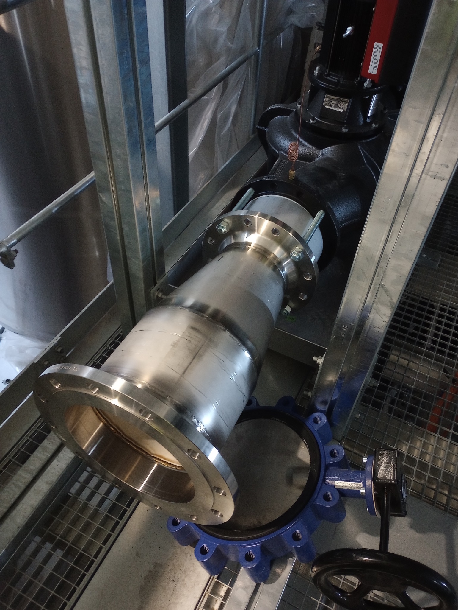 Instalacja przemysłowa z metalowymi rurami i zaworami w Będzieszynie. Elementy połączone spawami i śrubami, widoczne na tle metalowej konstrukcji.