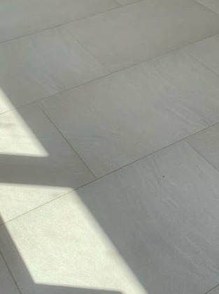 Jasnoszara kostka brukowa ułożona w regularny wzór, oświetlona naturalnym światłem tworzącym wyraźny cień. Widok z góry.