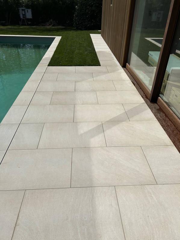 Jasne, prostokątne płyty chodnikowe ułożone obok basenu i budynku z drewnianą elewacją. W tle widoczny fragment trawnika. Minimalistyczny design.