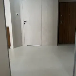 Jasna, gładka podłoga i ściany w odcieniach szarości, wykonane w Chotomowie. Minimalistyczne wnętrze z dwiema parami drzwi i zaokrąglonym narożnikiem ściany.