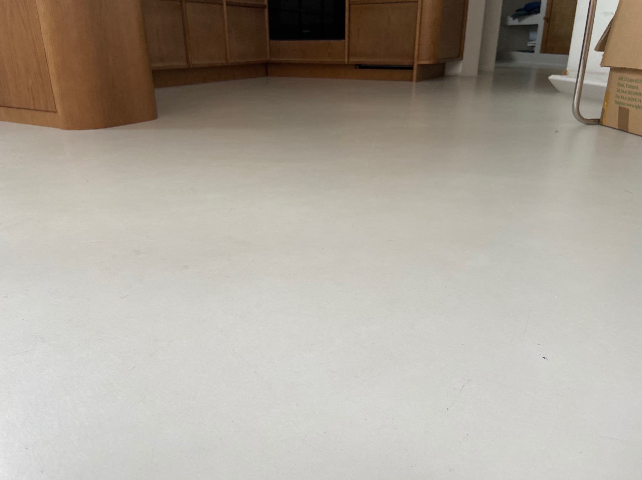 Jasna, gładka posadzka z mikrocementu w neutralnym odcieniu szarości, z widocznymi fragmentami zabudowy kuchennej i elementami wyposażenia wnętrza w tle.