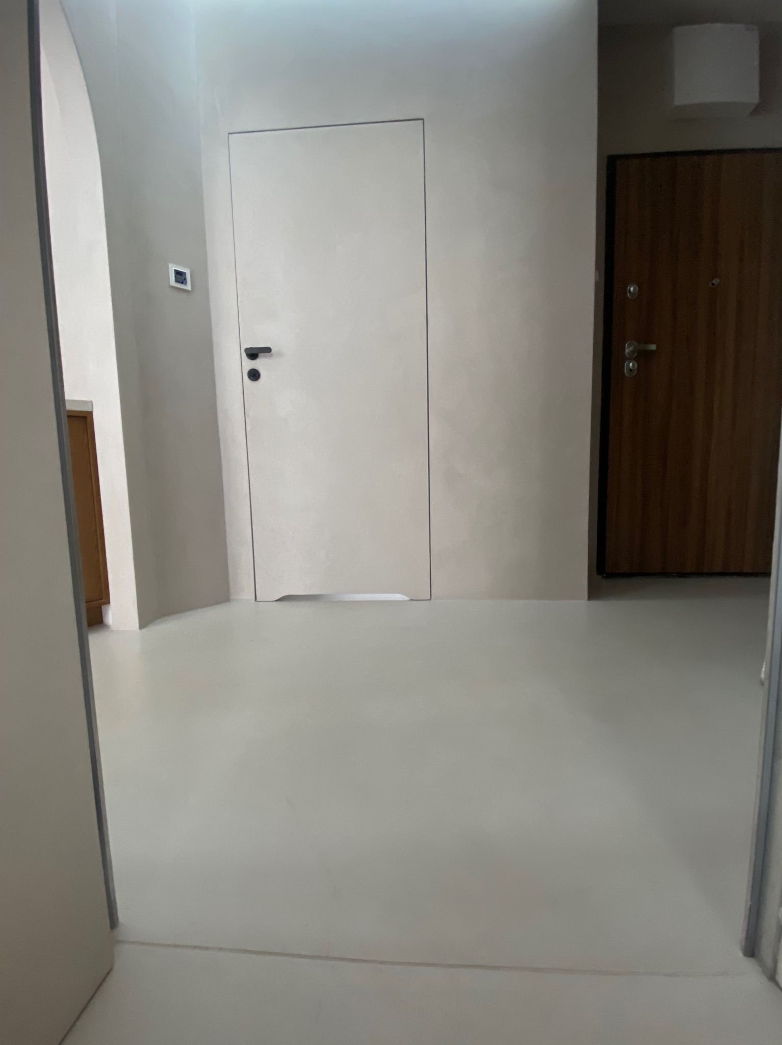 Jasna, gładka podłoga i ściany w odcieniach szarości, wykonane w Chotomowie. Minimalistyczne wnętrze z dwiema parami drzwi i zaokrąglonym narożnikiem ściany.