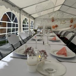 PYCHOTKA CAFE Jakub Pych - Uroczysty stół w białym namiocie: biały obrus, nakrycia, świece w szklanych świecznikach z jutowym sznurkiem, delikatne kwiaty, przezroczyste balony i dekoracje.