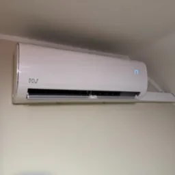 Biały klimatyzator ścienny z wyświetlaczem temperatury '17', zamontowany na jasnej ścianie w pomieszczeniu. Widoczne logo producenta.