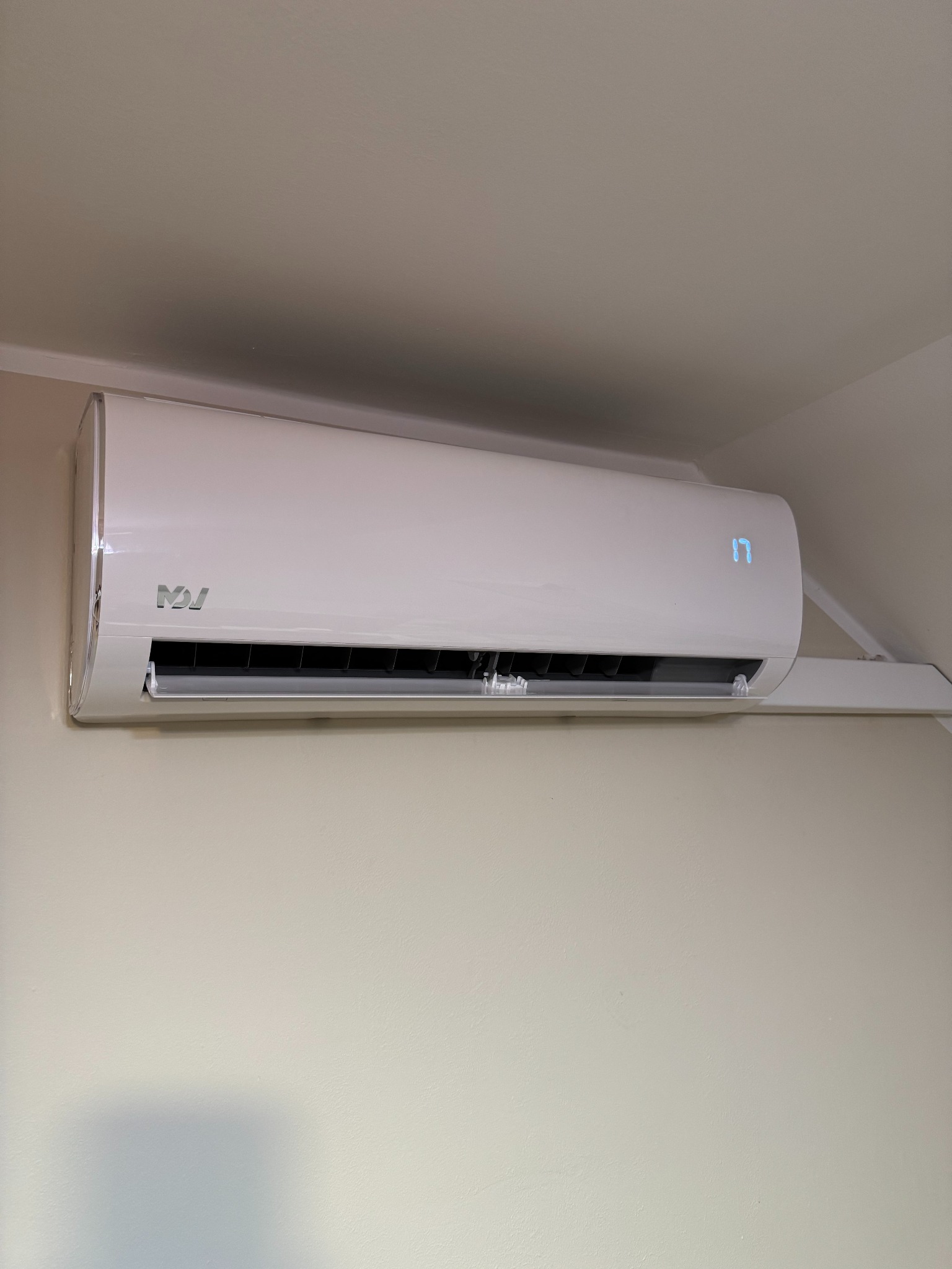 Biały klimatyzator ścienny z wyświetlaczem temperatury '17', zamontowany na jasnej ścianie w pomieszczeniu. Widoczne logo producenta.