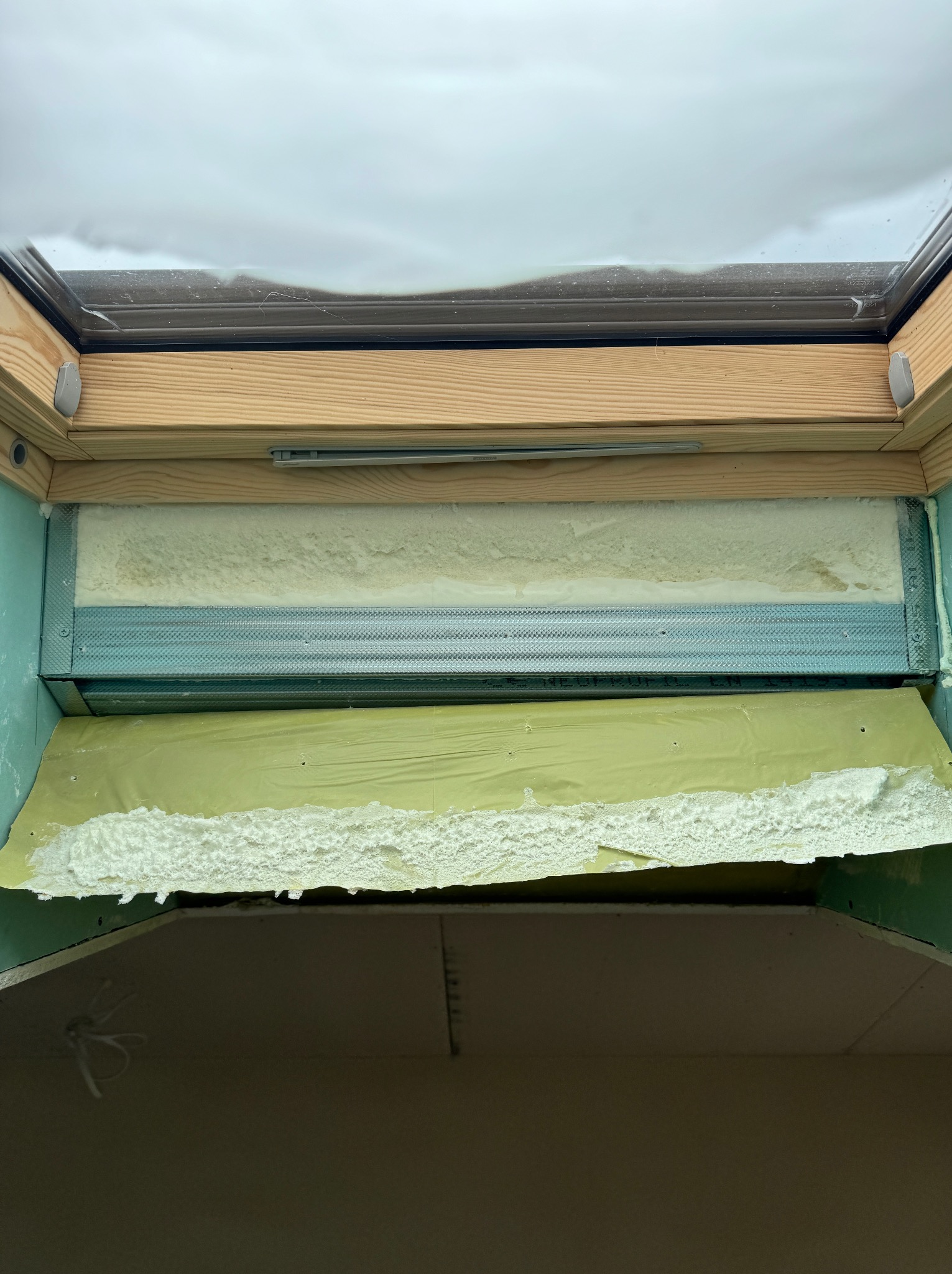 Ocieplenie poddasza pianką PUR wokół okna dachowego, widoczne elementy konstrukcyjne i izolacja w trakcie aplikacji.