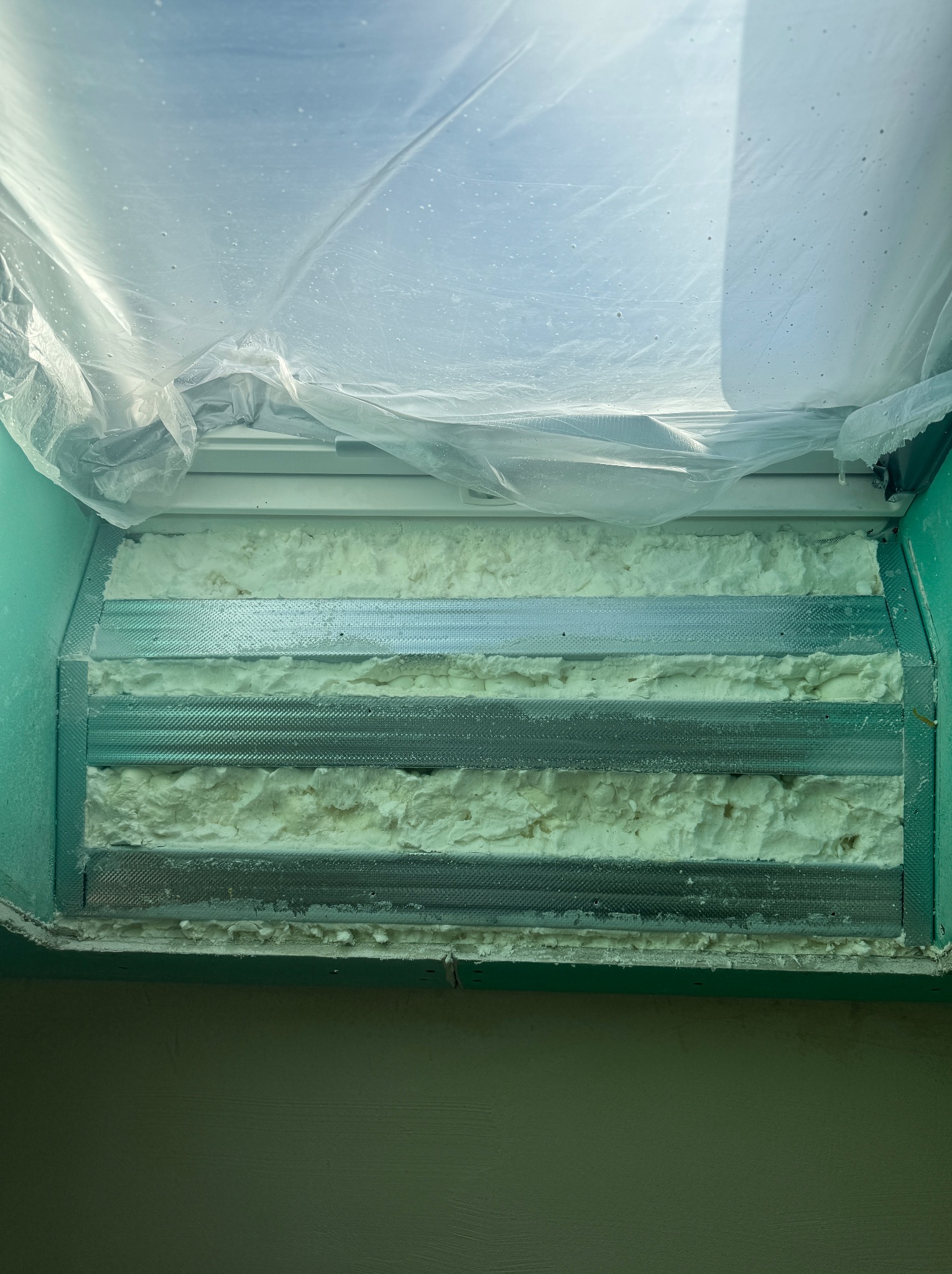 Ocieplanie poddasza pianką PUR, widoczne metalowe profile i wypełnienie pianką, zabezpieczone folią. Detal izolacji termicznej w trakcie prac.