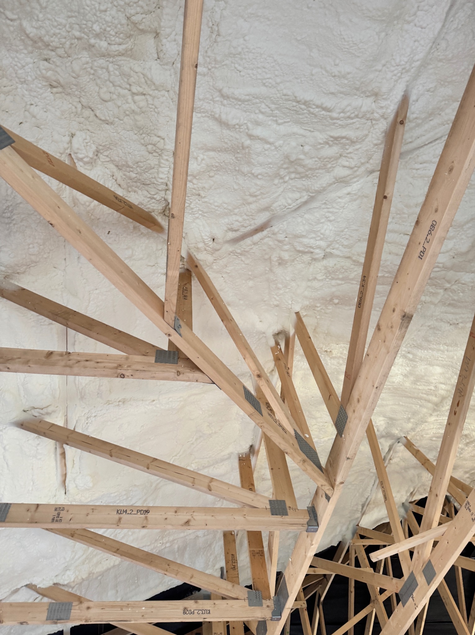 Poddasze ocieplone pianką PUR, widoczne drewniane elementy konstrukcyjne. Aplikacja pianki wypełnia przestrzeń między krokwiami, tworząc jednolitą warstwę izolacyjną.