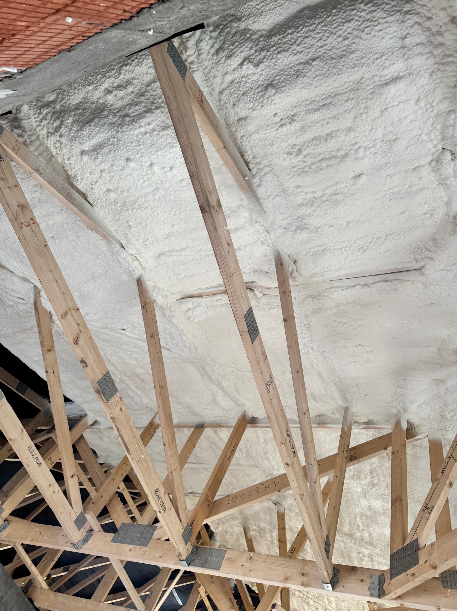 Poddasze po ociepleniu pianką PUR, widoczne drewniane krokwie i biała pianka wypełniająca przestrzeń. Widok z dołu.