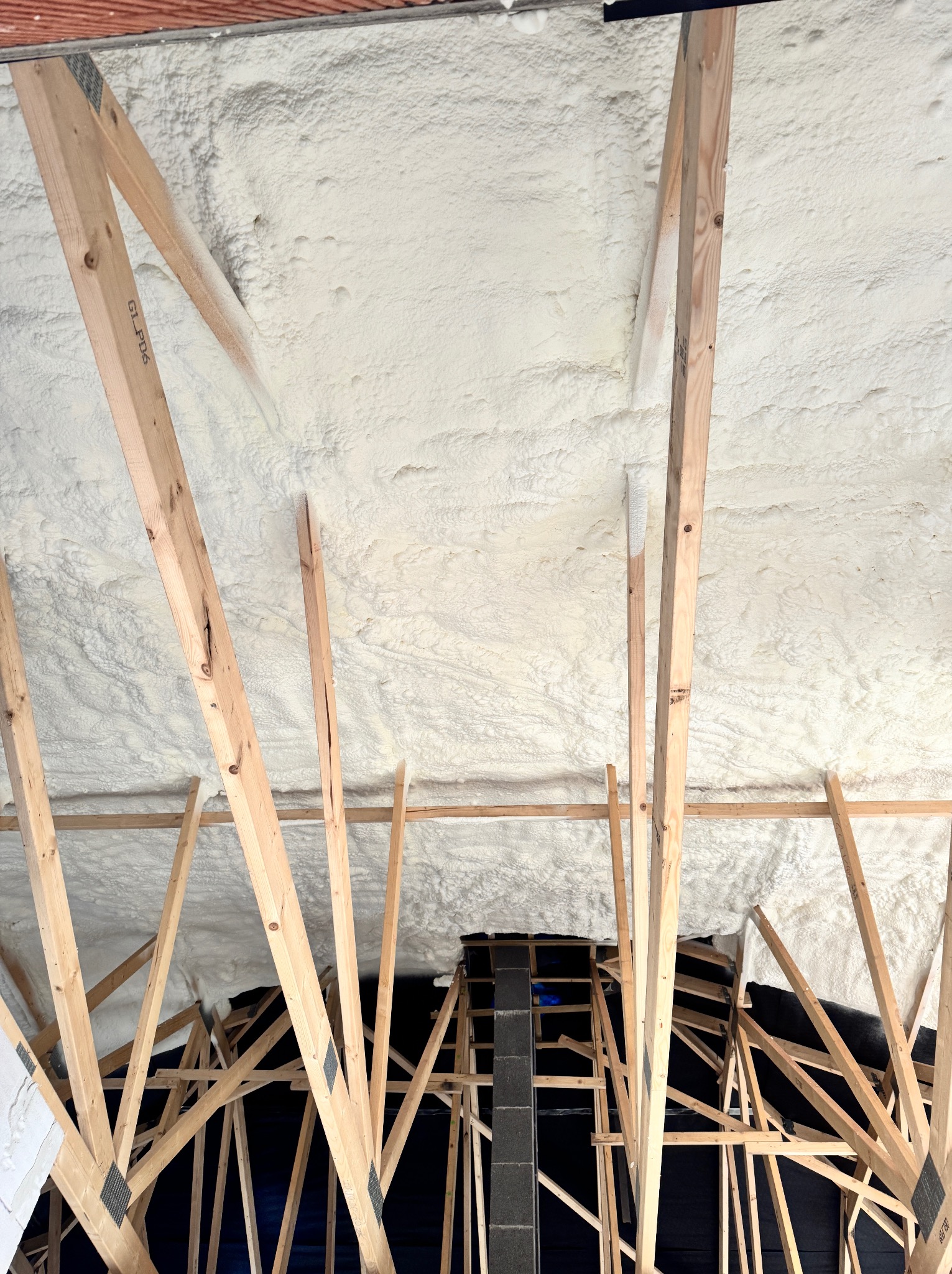 Poddasze ocieplone pianką PUR z widoczną drewnianą konstrukcją więźby dachowej. Czarny materiał izolacyjny w tle. Widok z dołu na ocieplenie poddasza.