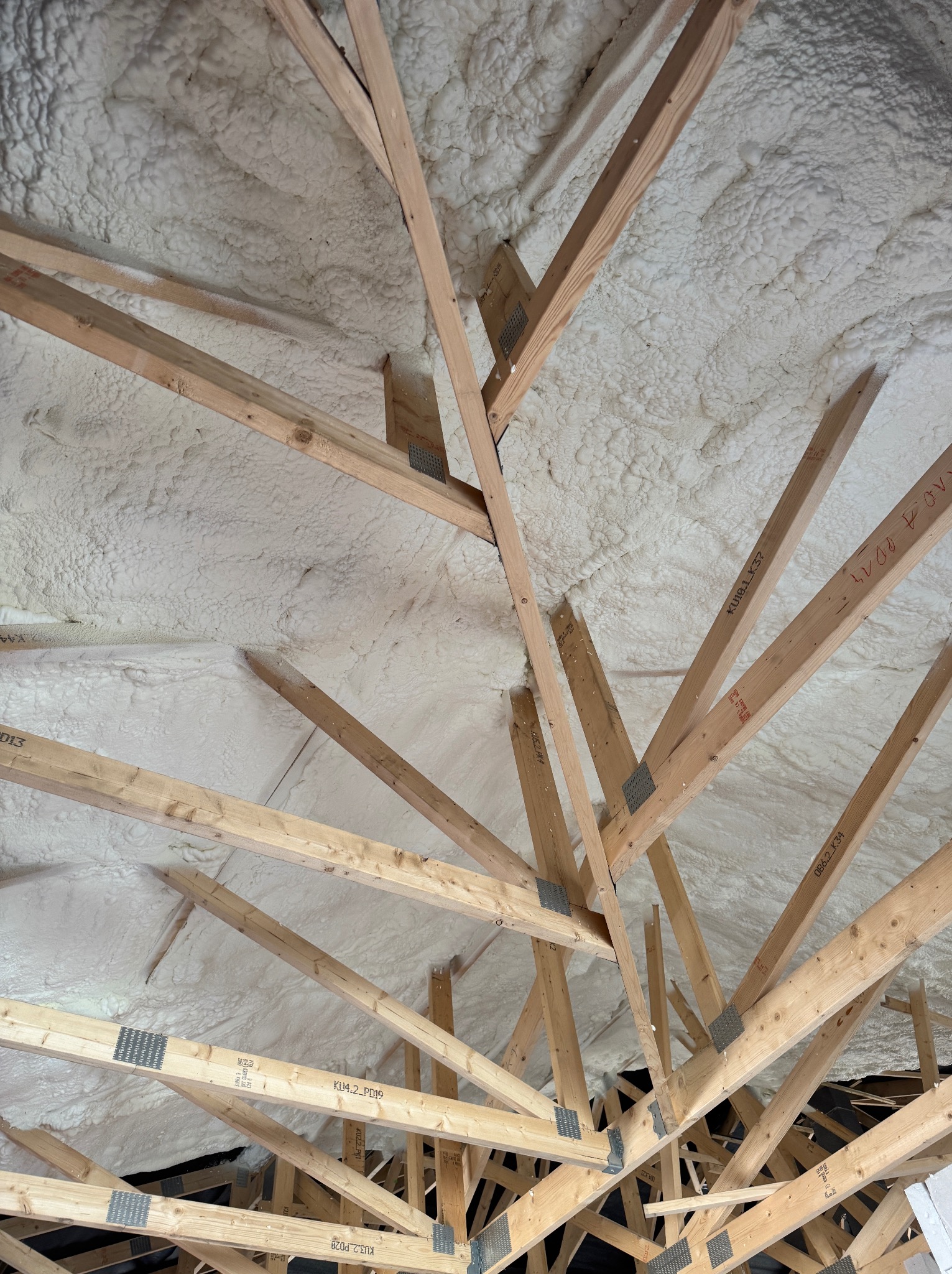 Skośny dach z drewnianą konstrukcją pokrytą białą pianką PUR, widoczne łączenia belek. Ocieplenie poddasza pianką poliuretanową.