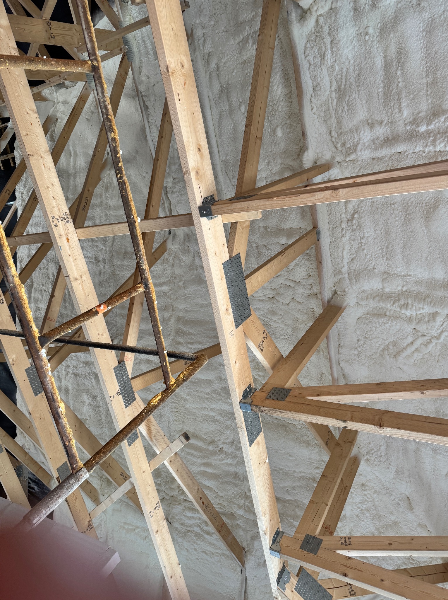Poddasze z drewnianą konstrukcją krokwiową i nałożoną warstwą jasnej pianki PUR, widoczne rusztowanie. Ujęcie od dołu.