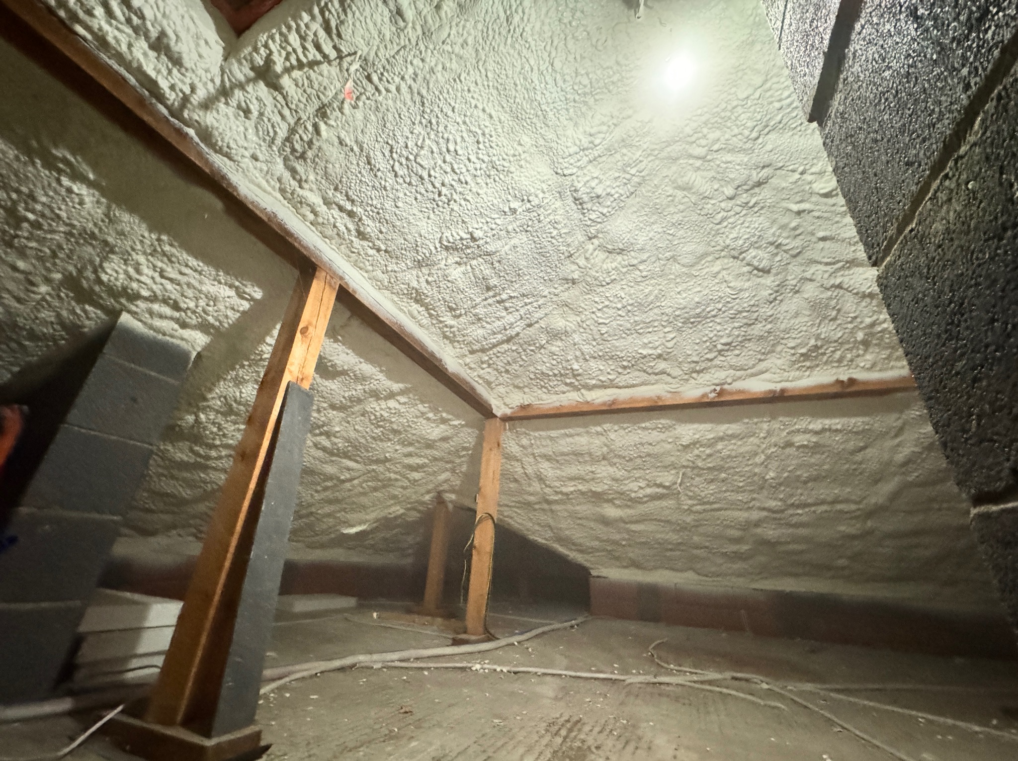 Poddasze po ociepleniu pianką PUR, widoczne drewniane elementy konstrukcyjne i szara ściana. Oświetlenie punktowe podkreśla strukturę pianki.