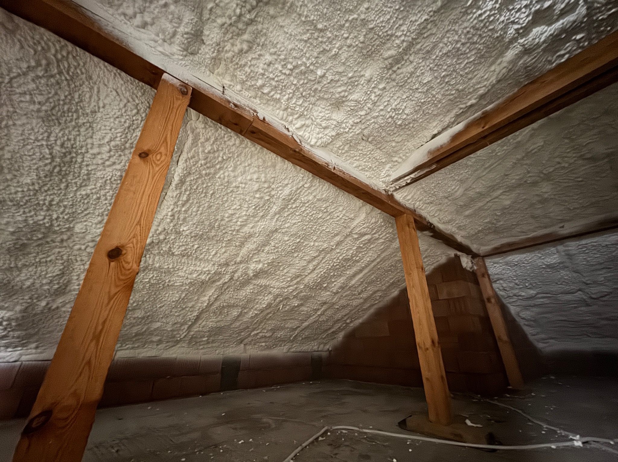 Poddasze po ociepleniu pianką PUR, widoczne drewniane elementy konstrukcyjne i nierównomierna struktura pianki na skośnych powierzchniach dachu.