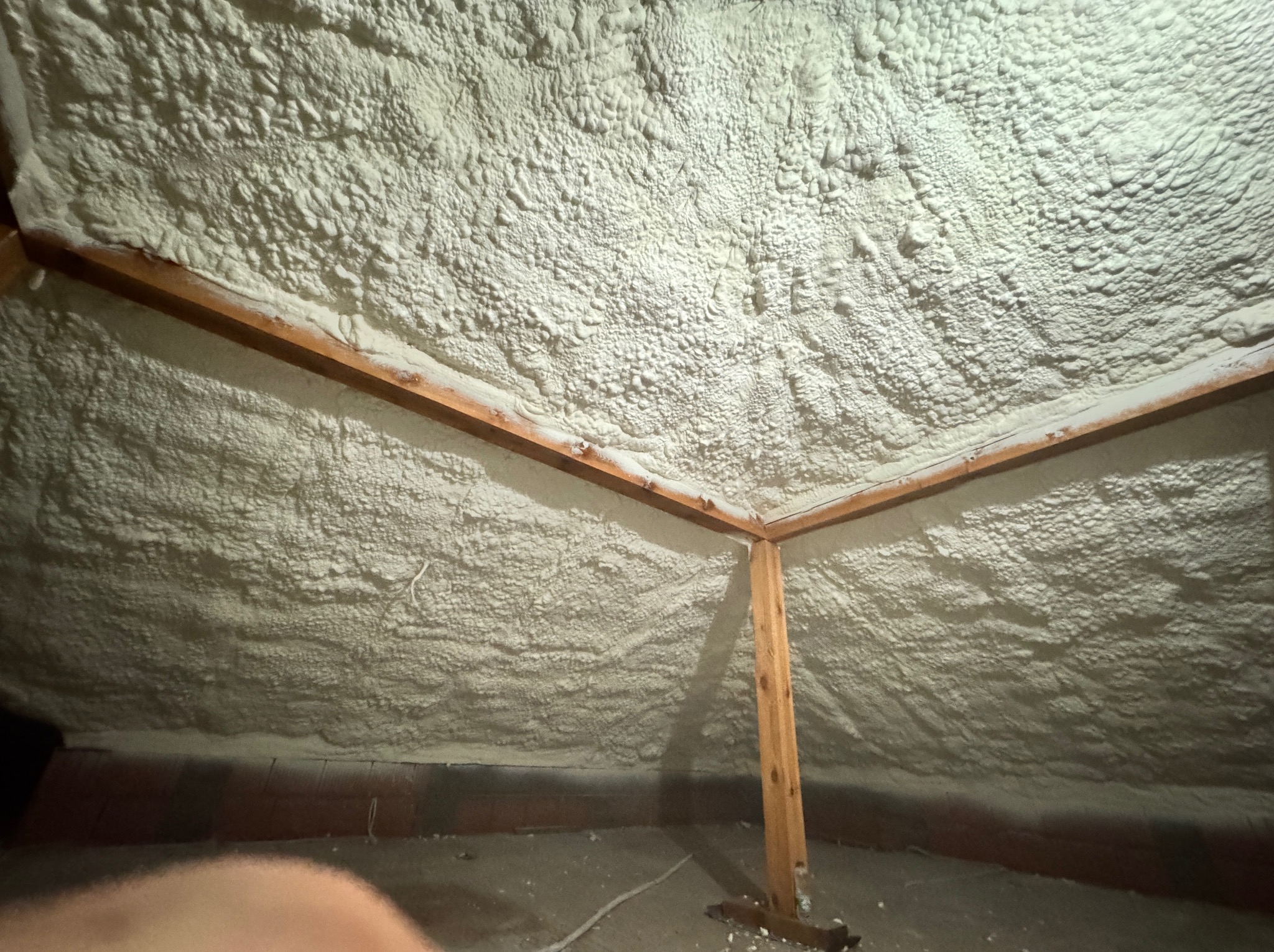 Poddasze po ociepleniu pianką PUR, widoczne drewniane elementy konstrukcyjne. Biała, nierówna powierzchnia pianki pokrywa całą przestrzeń.