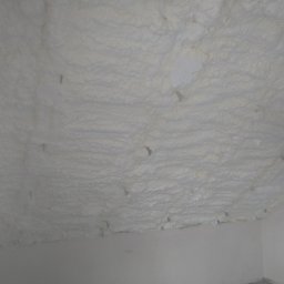 Sigma Pur - Poddasze po ociepleniu pianką PUR, widoczne nierównomierne pokrycie i wystające elementy mocujące. Biała izolacja wypełnia przestrzeń między krokwiami.