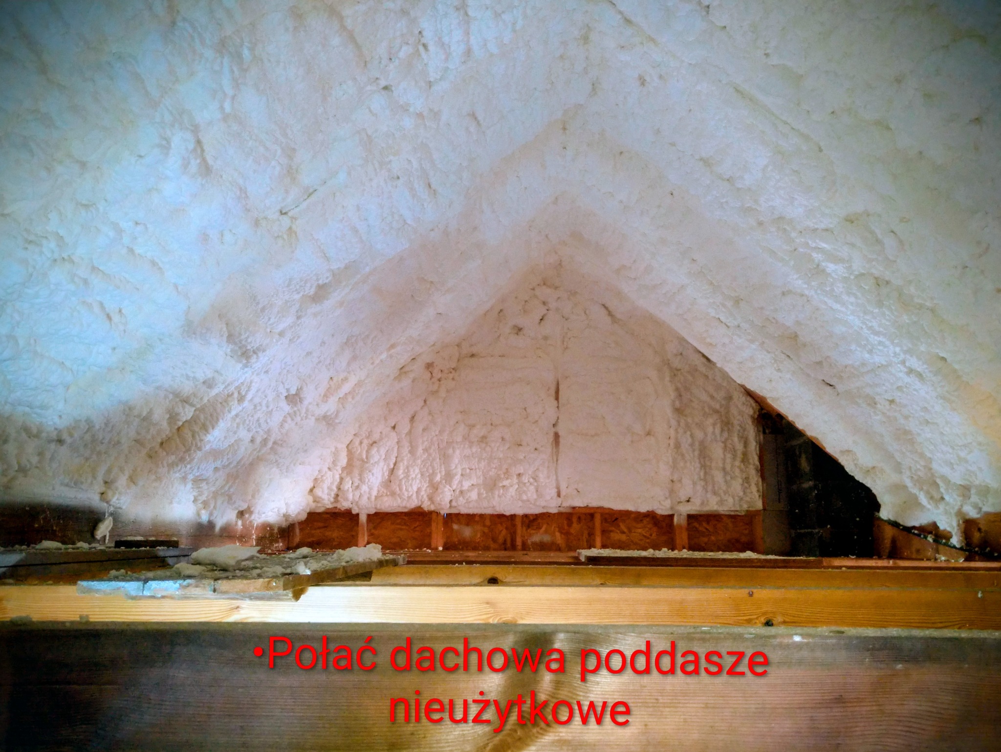 Poddasze nieużytkowe po ociepleniu pianką PUR, widoczne drewniane elementy konstrukcji dachu. Biała, nierówna powierzchnia izolacji wypełnia przestrzeń.