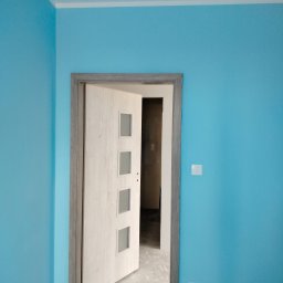 Mateusz - Świeżo pomalowane na błękitno ściany z zamontowanymi drzwiami z czterema szybkami i szarą futryną. Widoczny fragment gniazdka elektrycznego i włącznika.