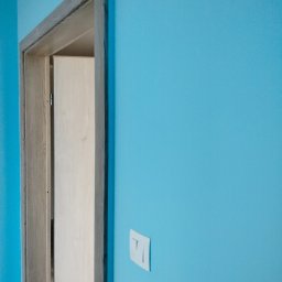 Mateusz - Turkusowa ściana z zamontowaną ościeżnicą drzwiową w surowym stanie i włącznikiem światła. Widok na wnętrze.