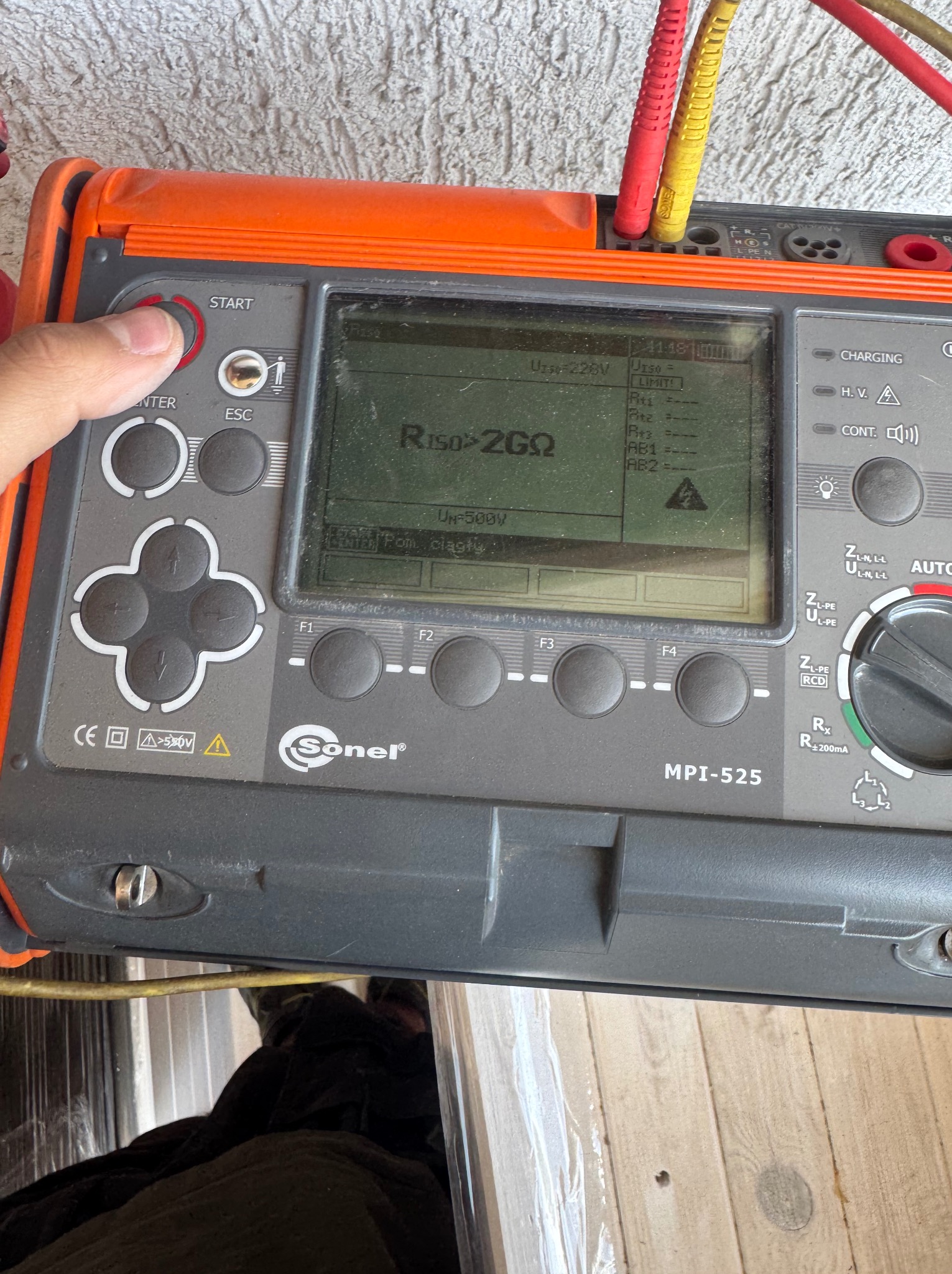 Miernik elektryczny Sonel MPI-525 w trakcie pomiaru, z widocznym ekranem i podłączonymi przewodami pomiarowymi. Palec naciska przycisk START.