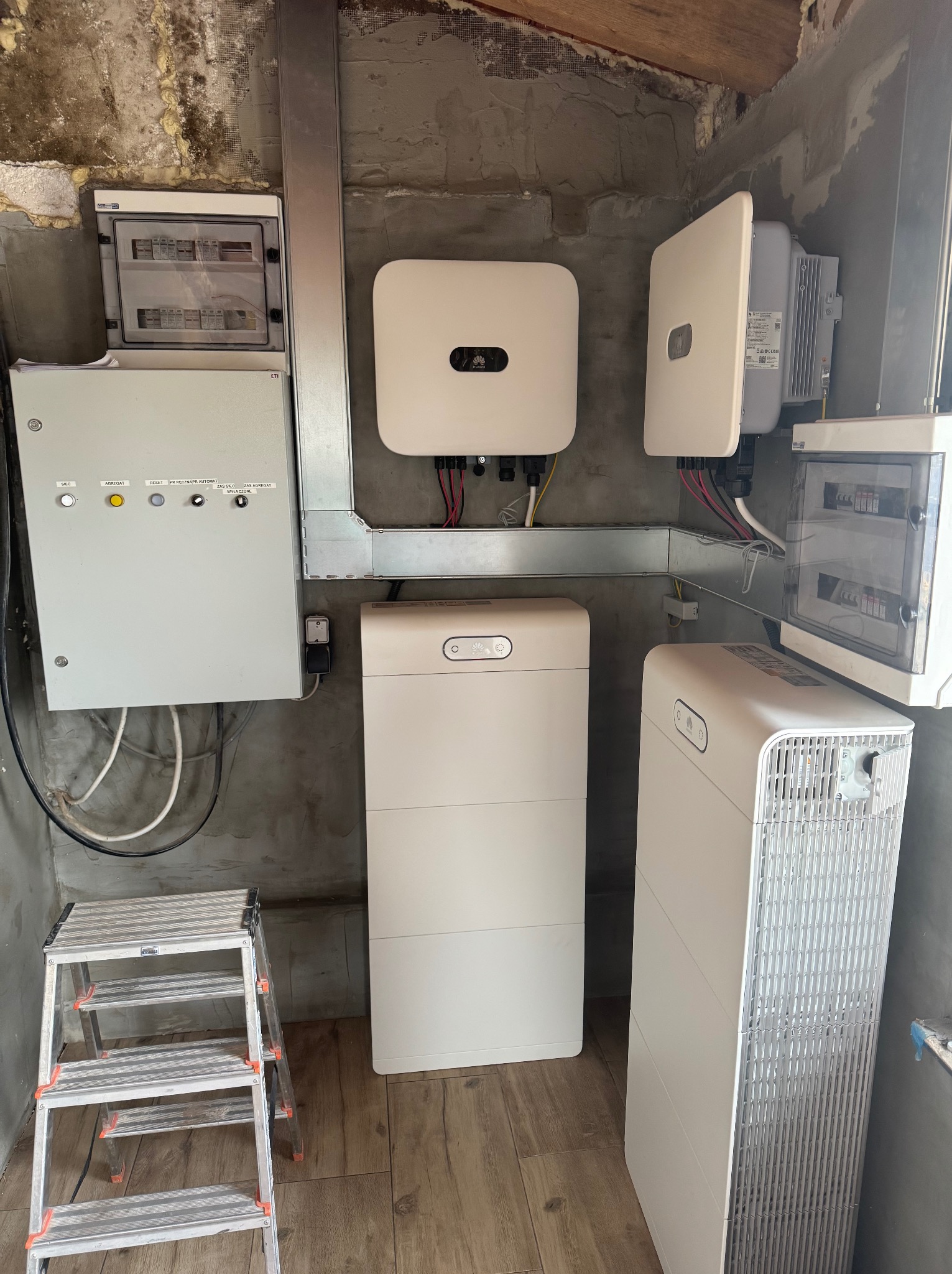 Kompleksowa instalacja systemu fotowoltaicznego w pomieszczeniu: rozdzielnice, inwertery Huawei i akumulatory energii. Widoczna drabina monterska.