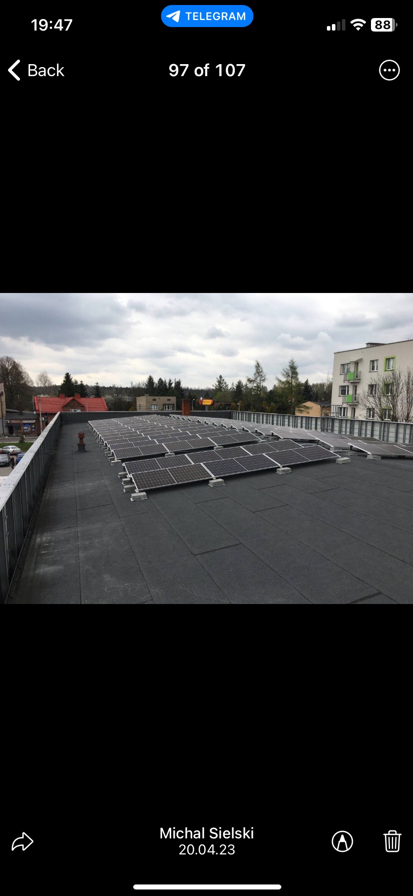 Rząd paneli słonecznych na płaskim dachu budynku w pochmurny dzień. Widok z góry, z widocznymi budynkami w tle. Instalacja fotowoltaiczna na dachu.