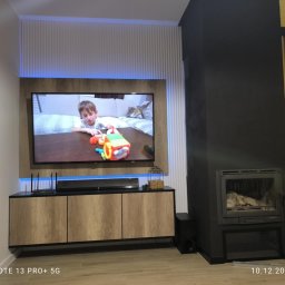 Meb-daw - Nowoczesna szafka RTV z drewnianymi frontami, podświetleniem LED i telewizorem, tworząca spójną zabudowę ściany w salonie z kominkiem i choinką.