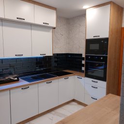 Meb-daw - Nowoczesna kuchnia z białymi frontami i drewnianymi akcentami. Czarne płytki nad blatem. Oświetlenie LED. Widoczne sprzęty AGD Samsung.