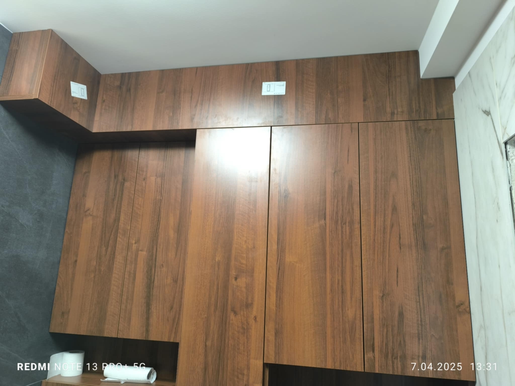 Drewniane szafki łazienkowe pod sufit, z widocznymi gniazdkami i rolkami papieru toaletowego w dolnej części. Ujęcie z dołu, ukazujące fakturę drewna.