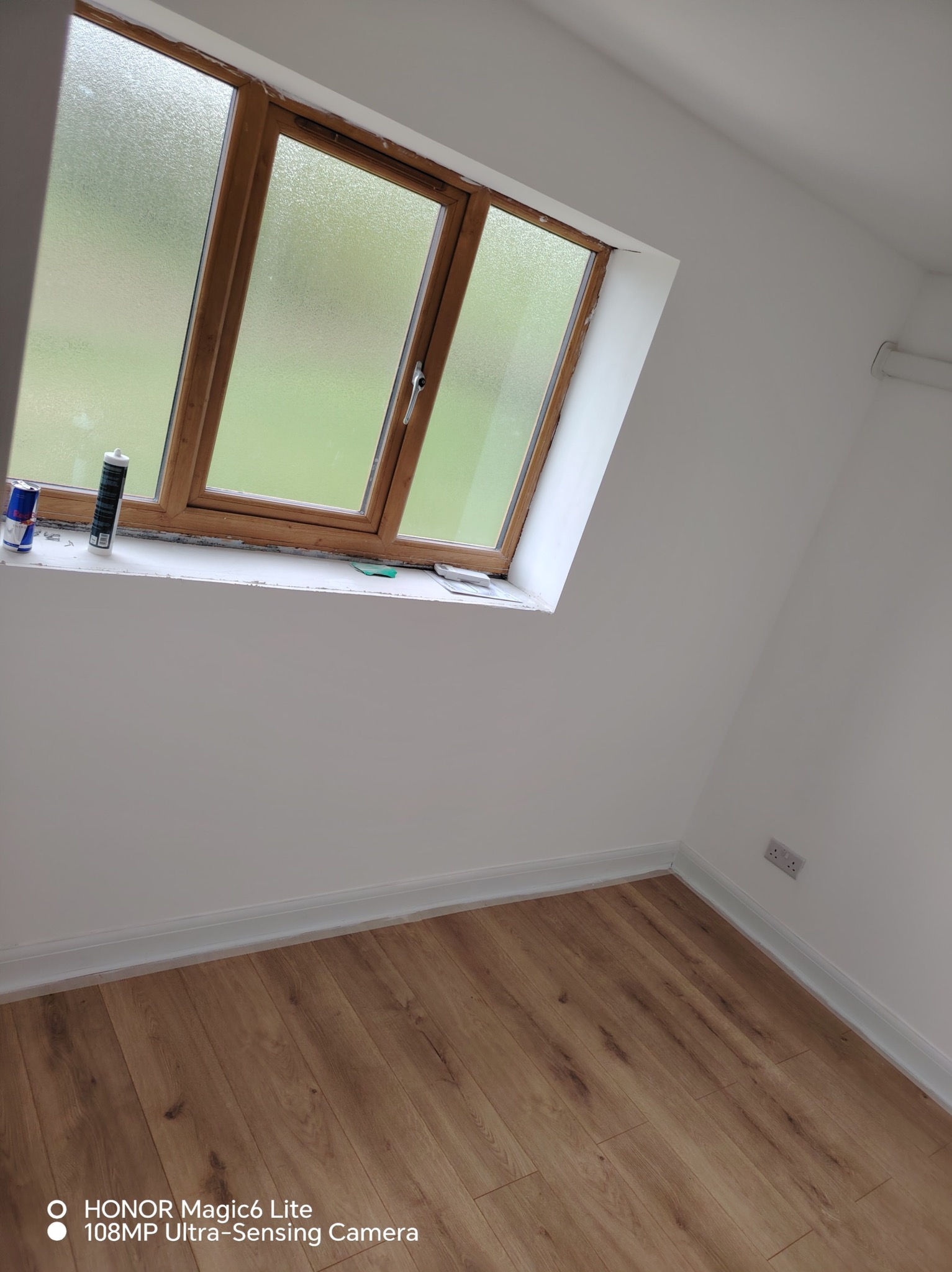 Wnętrze po remoncie: świeżo pomalowane ściany, drewniana podłoga, okno z drewnianą ramą, widoczne ślady prac wykończeniowych na parapecie.