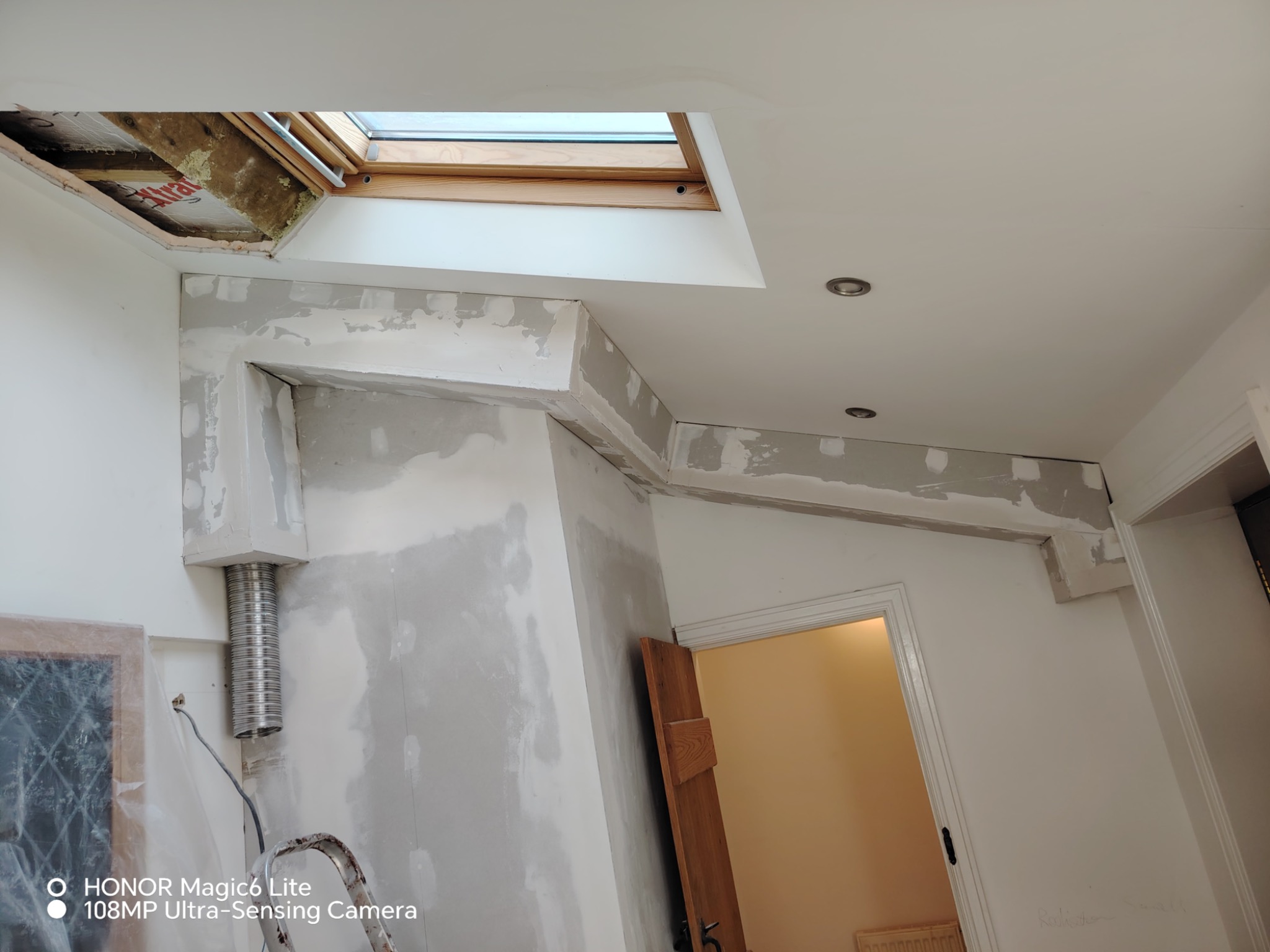 Wnętrze w trakcie prac wykończeniowych: ściany po szpachlowaniu, widoczne elementy instalacji wentylacyjnej, okno dachowe i fragment drabiny.