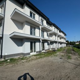 CHUKHACH GROUP POLSKA (CGP) SPÓŁKA Z OGRANICZONĄ ODPOWIEDZIALNOŚCIĄ - Nowoczesny budynek wielorodzinny z balkonami, świeżo po malowaniu elewacji na biało i szaro, w słoneczny dzień. Widok z dołu, podkreślający geometrię budynku.