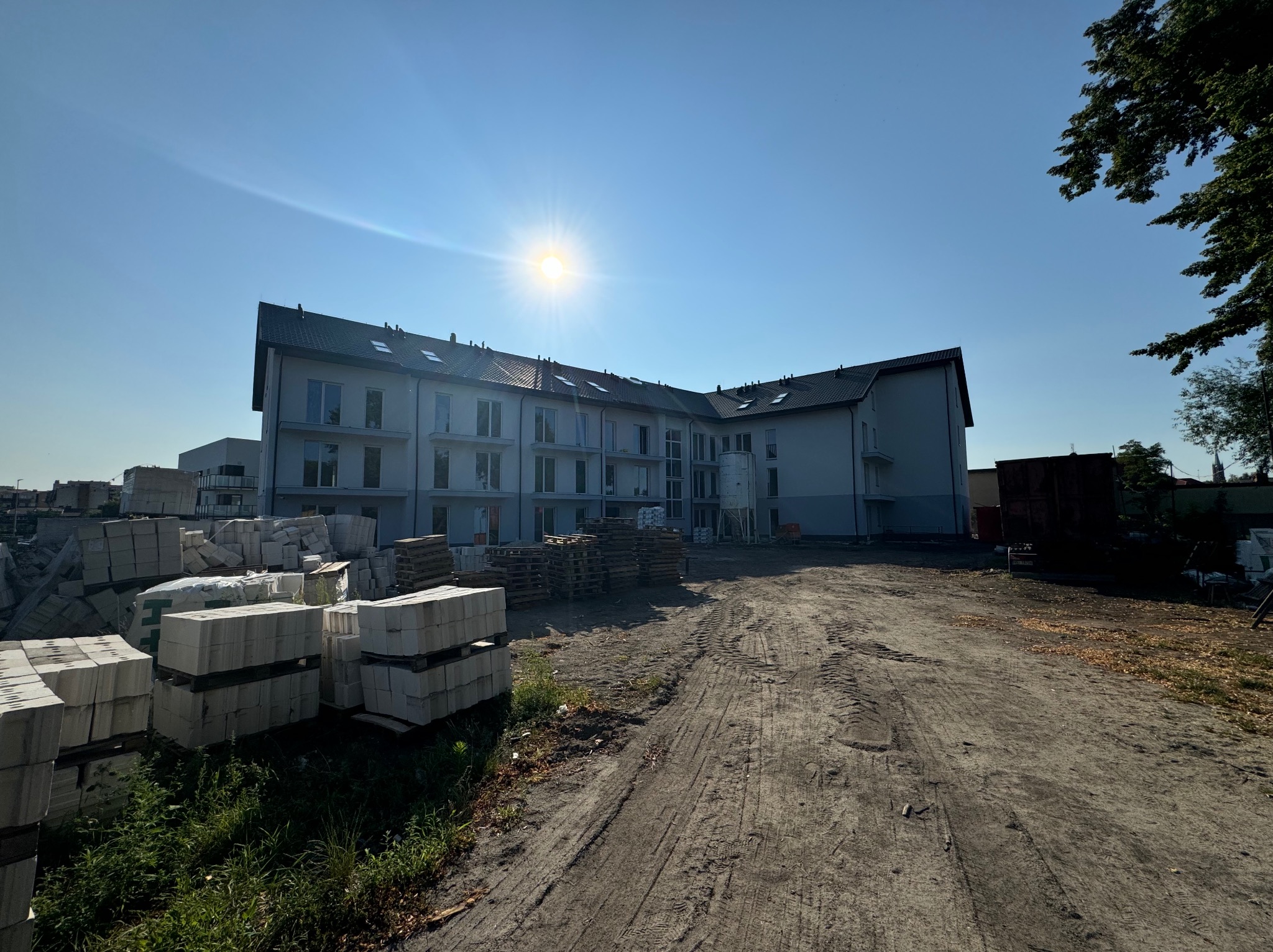 Nowoczesny budynek wielorodzinny w trakcie budowy, widok z dołu na jasną elewację i materiały budowlane na placu. Słoneczny dzień.