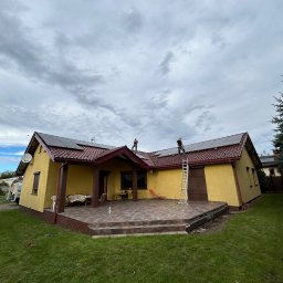 VoltMaster PAWEŁ MIŚKIEWICZ - Żółty dom z panelami słonecznymi na dachu, montowanymi przez dwóch pracowników z użyciem drabiny. Pochmurne niebo w tle. Widok z poziomu trawnika.