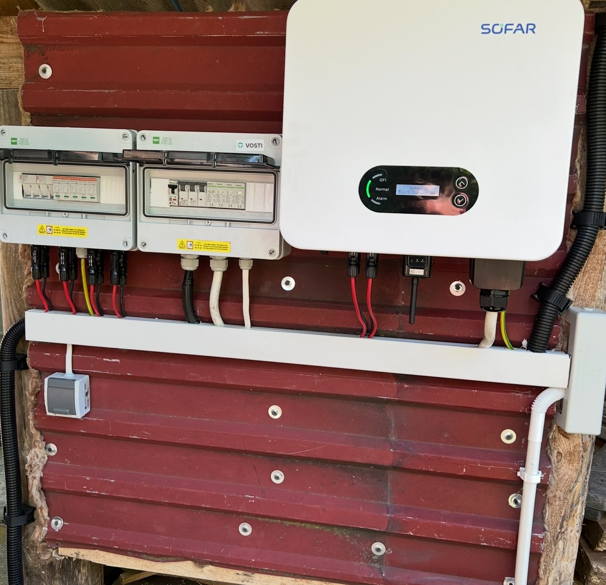 Instalacja fotowoltaiczna SOFAR z rozdzielnicami VOSTI na czerwonej, drewnianej ścianie. Widoczne przewody i zabezpieczenia.