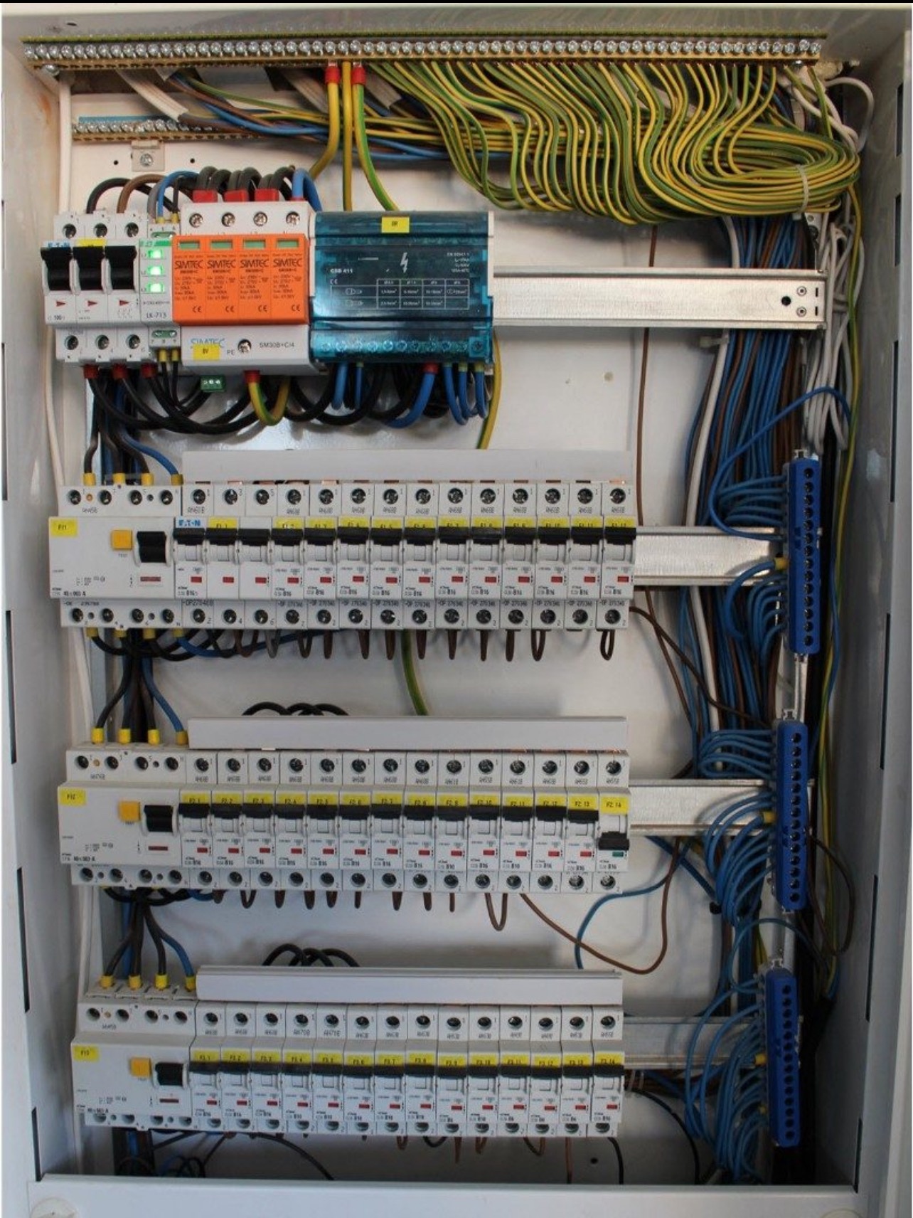 Rozdzielnia elektryczna z widocznymi zabezpieczeniami, przewodami o różnych kolorach i listwami zaciskowymi. Widok z bliska na wnętrze skrzynki elektrycznej.